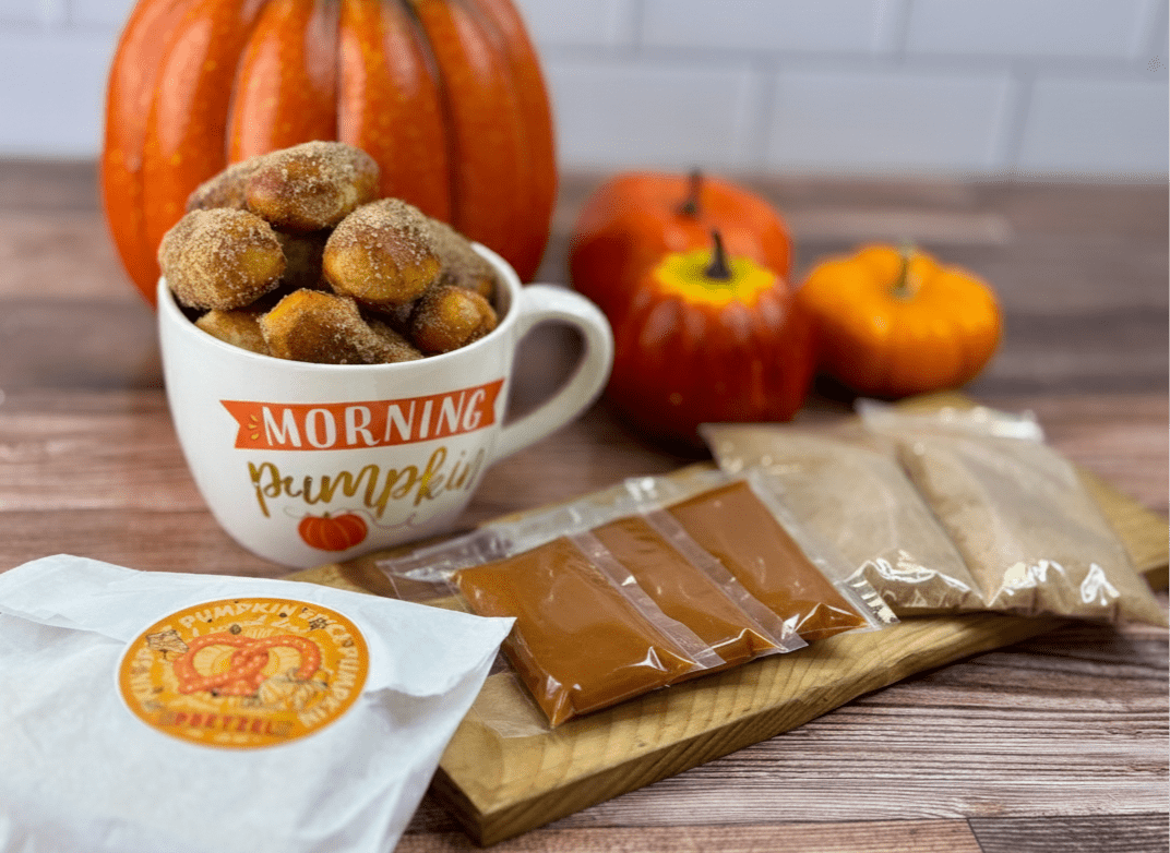 Cup of donuts with 'Morning Pumpkin' text, pumpkins, and packets on a wooden surface
