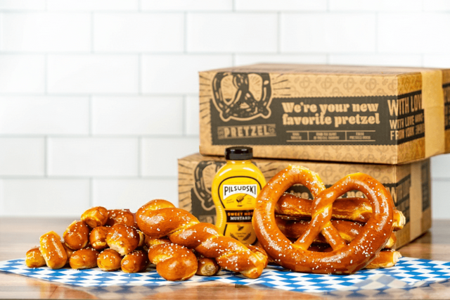 Pretzel and mustard bottle on a checkered cloth with branded boxes in the background.